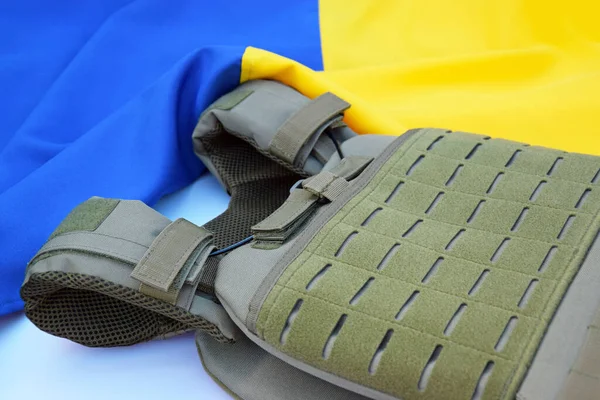 Tactical, military body armor with plates on the background of the flag of Ukraine. The concept of protecting the body from shots in the war in Ukraine.