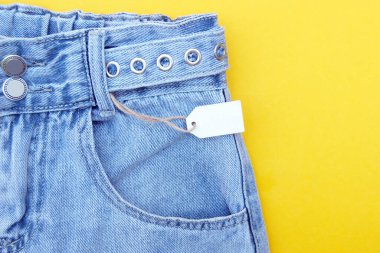 Düz yatış, kot pantolon ayrıntıları, sarı arka planda beyaz etiketler. Alışveriş ve indirim konsepti. Kara Cuma.