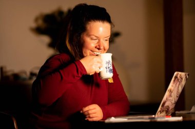 Dizüstü bilgisayarı ve kahvesi olan genç bir kadın.