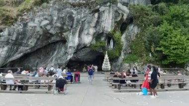 Lourdes, Fransa - 28 Ağustos 2021: Kutsal mağaranın önünde dua eden hacılar - Marian hayaletlerinin olduğu Lourdes 'te mağara. Gimbal hareketi.