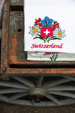 Appenzell, İsviçre - 27 Mayıs 2022: Alp çiçekleri motifli hediyelik peçete ve antik ahşap bir el arabasına İsviçre yazması