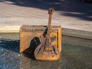 Lozan, İsviçre - 14 Temmuz 2022: İsviçre 'nin Lozan kentinde bir su çeşmesinde gitar amplifikatörü ve elektro gitarın sanatsal temsili