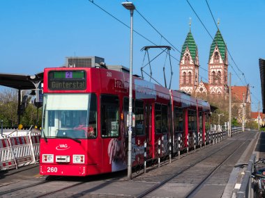 Freiburg im Breisgau, Almanya - 13 Nisan 2022: Kutsal Yürek Kilisesi manzaralı tramvay durağında kırmızı tramvay