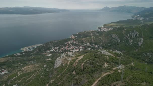 Una vista del dron de una carretera de montaña y una pequeña ciudad costera en la región de Makarska Riviera de Croacia llamada Krvavica, con la impresionante costa adriática y la isla de Brac en el fondo. — Vídeos de Stock