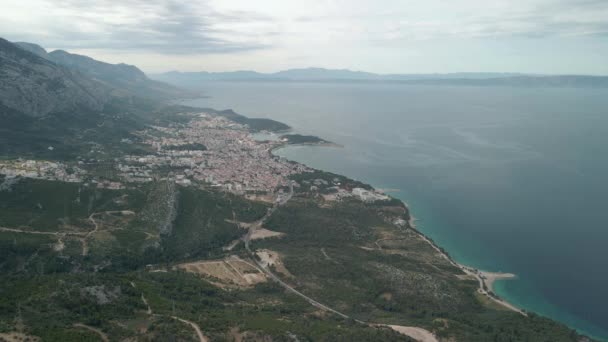 Drone vista de una carretera de montaña en la región de Makarska Riviera en Croacia, con impresionantes costas adriáticas y la ciudad de Makarska en el fondo. — Vídeo de stock
