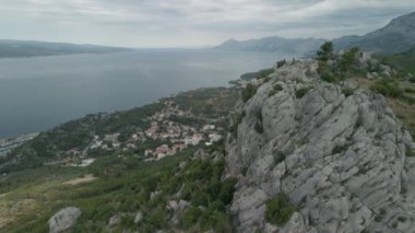 İnsansız hava aracı Hırvatistan kıyısındaki küçük bir kasabanın arka planında büyük bir kayanın yanından geçiyor. Makarska Riviera bölgesi, Krvavytsia kasabası.
