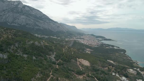 Drone pohled na horskou silnici v regionu Makarské riviéry v Chorvatsku, s ohromující pobřeží Jaderského moře a město Makarska v pozadí. — Stock video