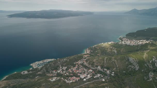 Uma visão drone de uma estrada de montanha e uma pequena cidade costeira na região de Makarska Riviera, na Croácia, chamada Krvavica, com deslumbrante costa adriática e a ilha de Brac ao fundo. — Vídeo de Stock