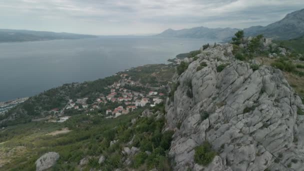 Drone vliegt langs een grote rots tegen de achtergrond van een klein stadje aan de kust van Kroatië. Makarska Riviera, stad Krvavytsia. — Stockvideo