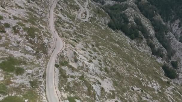 两个骑自行车的人在蜿蜒在山坡上的一条狭窄的蛇形路上擦肩而过，背景是一副奇景. — 图库视频影像