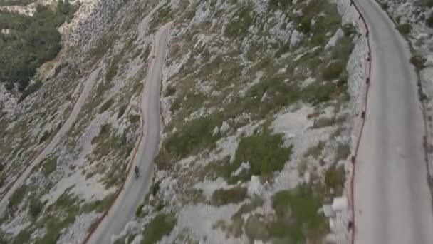 Велосипедист спускается по узкой трассе, извиваясь по склону самой высокой горы в природном парке Биоково Хорватия. — стоковое видео