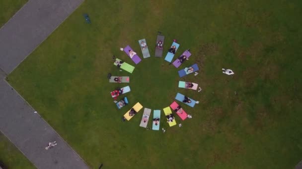 Aerial view of a large group of women doing gymnastics sitting on mats. Karemats are arranged in a circle on site. — Stockvideo