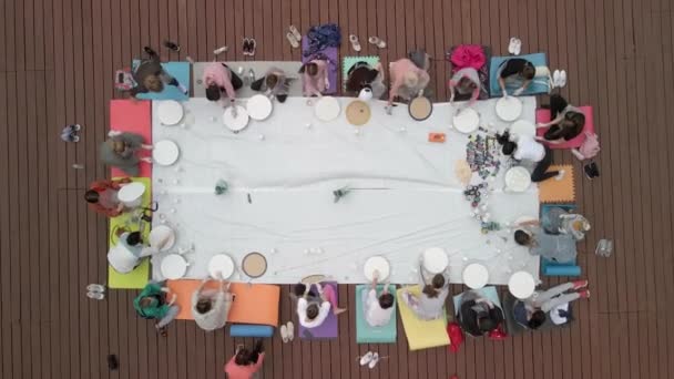 Aerial view of a group of women and children engaged in creativity on a wooden terrace in the open air. Painting. — Stok video