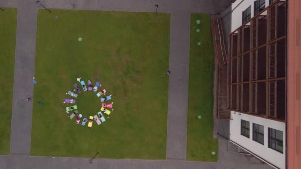 Aerial view of a large group of women doing gymnastics sitting on mats. Karemats are arranged in a circle on site. — Vídeo de Stock
