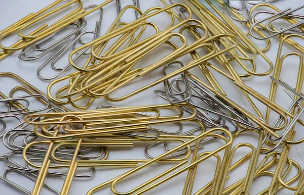 Gold and silver colourd paper clips in a pile on a white background.