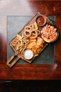 Deniz ürünleri birası aperatifleri. Kızarmış balık, patates kızartması, karides, kalamar halkaları, limon dilimi, domates sosu ve tartar sosu. Üst görünüm