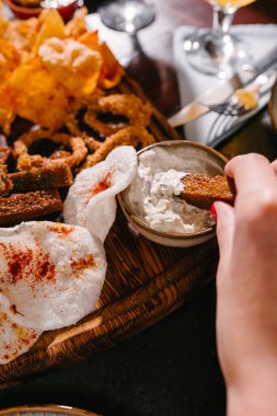 Kız sosa kraker batırıyor. Patates ve pirinç cipsi, kızarmış ekmek, soğan halkaları, füme peynir, domates sosu, tartar sosu..