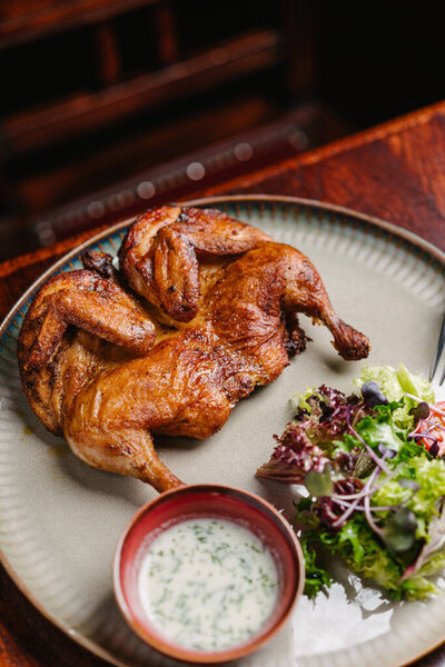 Grilled fried roast Chicken Tabaka with garlic sauce and salad on a wooden table