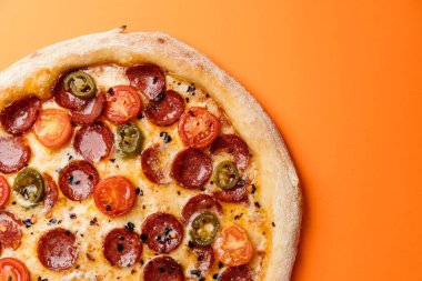 Tütsülenmiş sosisli pizza, vişneli domates, kurutulmuş kırmızı biber, biber ve mozzarella. Turuncu arka plan. Üst Manzara. Boşluğu kopyala
