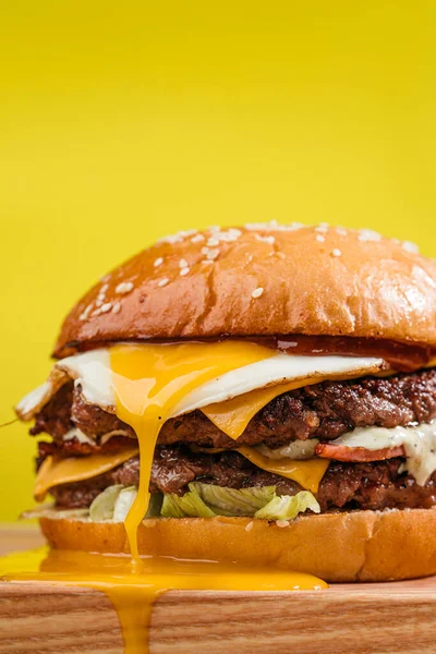 Çift köfteli burger, mermer biftek, pastırma, çedar peyniri, yumurta sarısı, domates, onios, krem sosu ve ketçap. Tahta masa, sarı arka plan. Kapat.