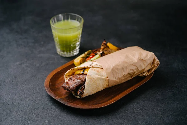 Plant-based meat kebab in lavash on a wooden plate with grilled vegetables and juice on a dark concrete background. copy space