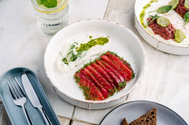 Gravlax, İskandinav kurutulmuş somon beyaz tabakta feta mus ve mantar soslu dana tartar ve salatalık turşusu.