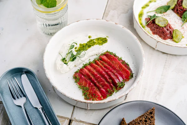 Gravlax, İskandinav kurutulmuş somon beyaz tabakta feta mus ve mantar soslu dana tartar ve salatalık turşusu.
