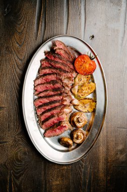 Izgara sebze garnitürlü kemiksiz biftek, demir tepsi, ahşap masa. en üstteki görünüm