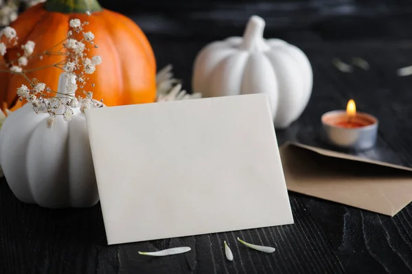 Mock-up card with Craft envelope, white paper and pumpkins on black wooden background. Still life with copyspace for text. Autumnal greeting card and advertisment