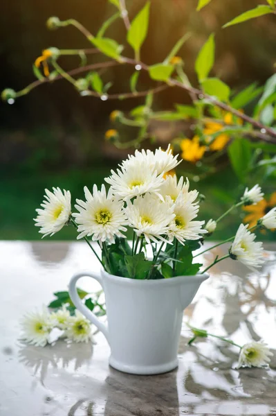 White chrysanthemum in vase on wet marble table in garden. Rainy day outdoor