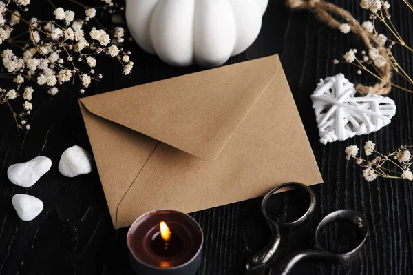 Mock-up card with craft brown envelope and heart and dry flowers on black wooden background. Still life with copyspace for text. Autumnal greeting card and advertisment