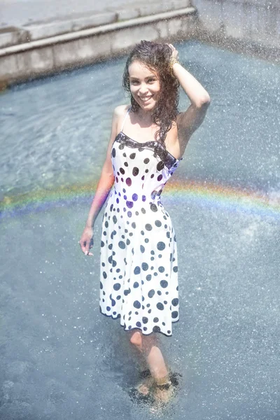 Femme en robe humide et cheveux bruns mouillés posant sur le fond de l'arc-en-ciel de la fontaine — Photo