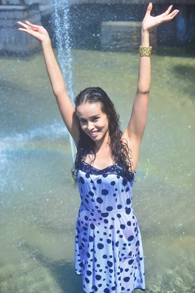 Ragazza allegra con le mani alzate in un vestito bagnato e capelli castani in posa sullo sfondo della fontana — Foto Stock