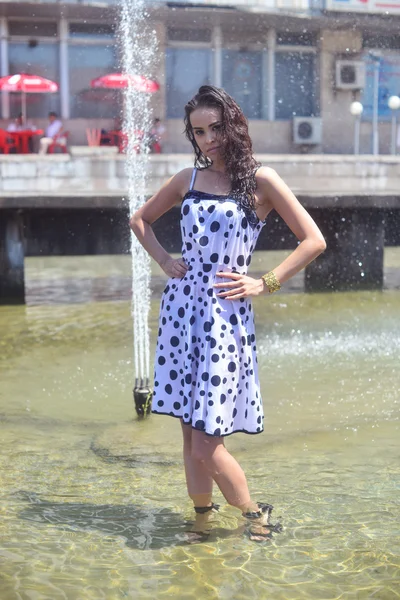 Belle femme aux cheveux bruns, un joli visage et une bonne figure posant sur le fond de la fontaine — Photo