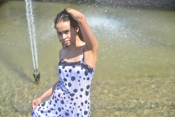 Smiling girl in a wet dress and wet hair posing in the water at the fountain — Stock Photo, Image