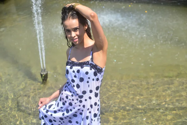 Menina sorridente em um vestido molhado e cabelo molhado posando na água na fonte — Fotografia de Stock