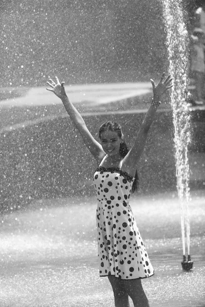 Chica alegre con las manos levantadas en un vestido mojado y cabello castaño posando en el fondo de la fuente —  Fotos de Stock