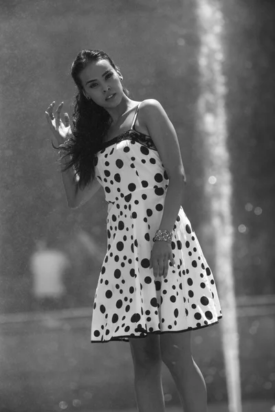 Woman on the background of the fountain in summer dress touching hair — Stock Photo, Image