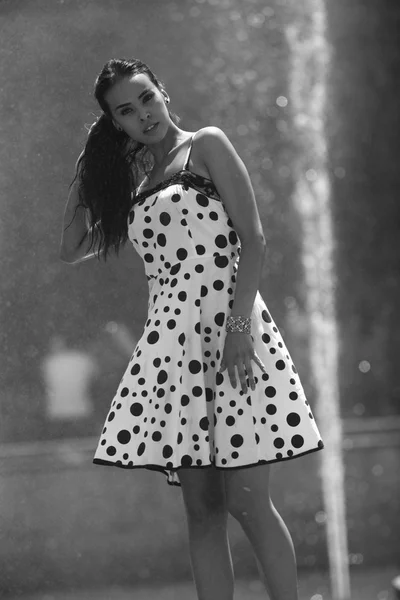 Жінка на фоні фонтану в літній сукні торкається волосся — стокове фото