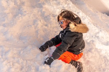 Kar oynayan çocuk. Kışın güneş gözlüğü ve eldiven takan Asyalı bir kız. Mutlu çocukluk.