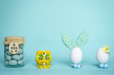Yumurtalı Paskalya tavşanı. Mavi arka planlı komik bir dekorasyon. Mutlu Paskalyalar. Sarı çiçekli beyaz yumurta.