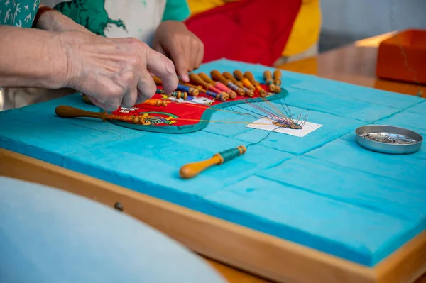 Hands making bobbin lace. Adult helps child learn craft. Colorful lace threads. Skill and creativity.