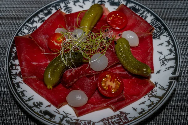 Sliced dried meat, pickled cucumber and onions. Food appetizer concept. Traditional Swiss food. Delicious.