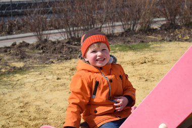 Kaydırağın yanındaki parkta gülümseyen küçük bir çocuğun portresi..