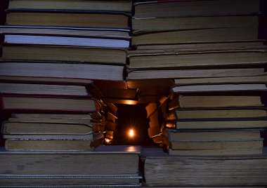 Kitap yığınları ve arkalarında bir ışık kaynağı. Bilginin ışığı için çabalama kavramı.