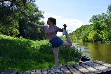Genç bir kadın nehir kıyısında egzersiz yapıyor..