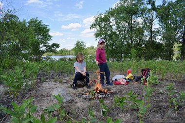Bir oğlan ve bir kız nehir kıyısında ateşte sosis kızartırlar..