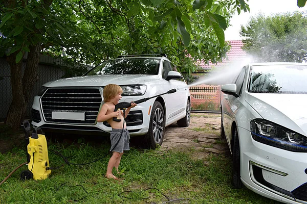 A little boy is washing a car with a pressure washer.