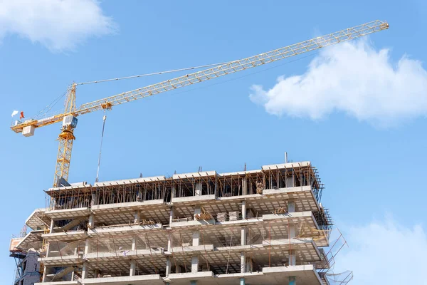 Bitmemiş bir binanın arka planında inşaat vinci ve bulutlu mavi bir gökyüzü..