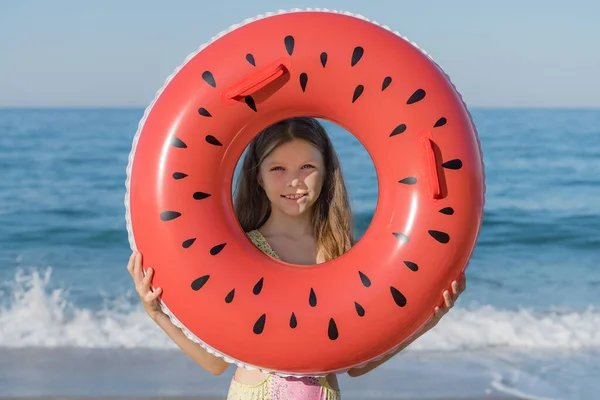 A young girl looks through an inflatable ring on the beach. Summer holidays on the sea coast.